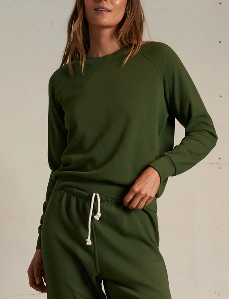 Woman wearing a green sweatshirt and pants against a plain background